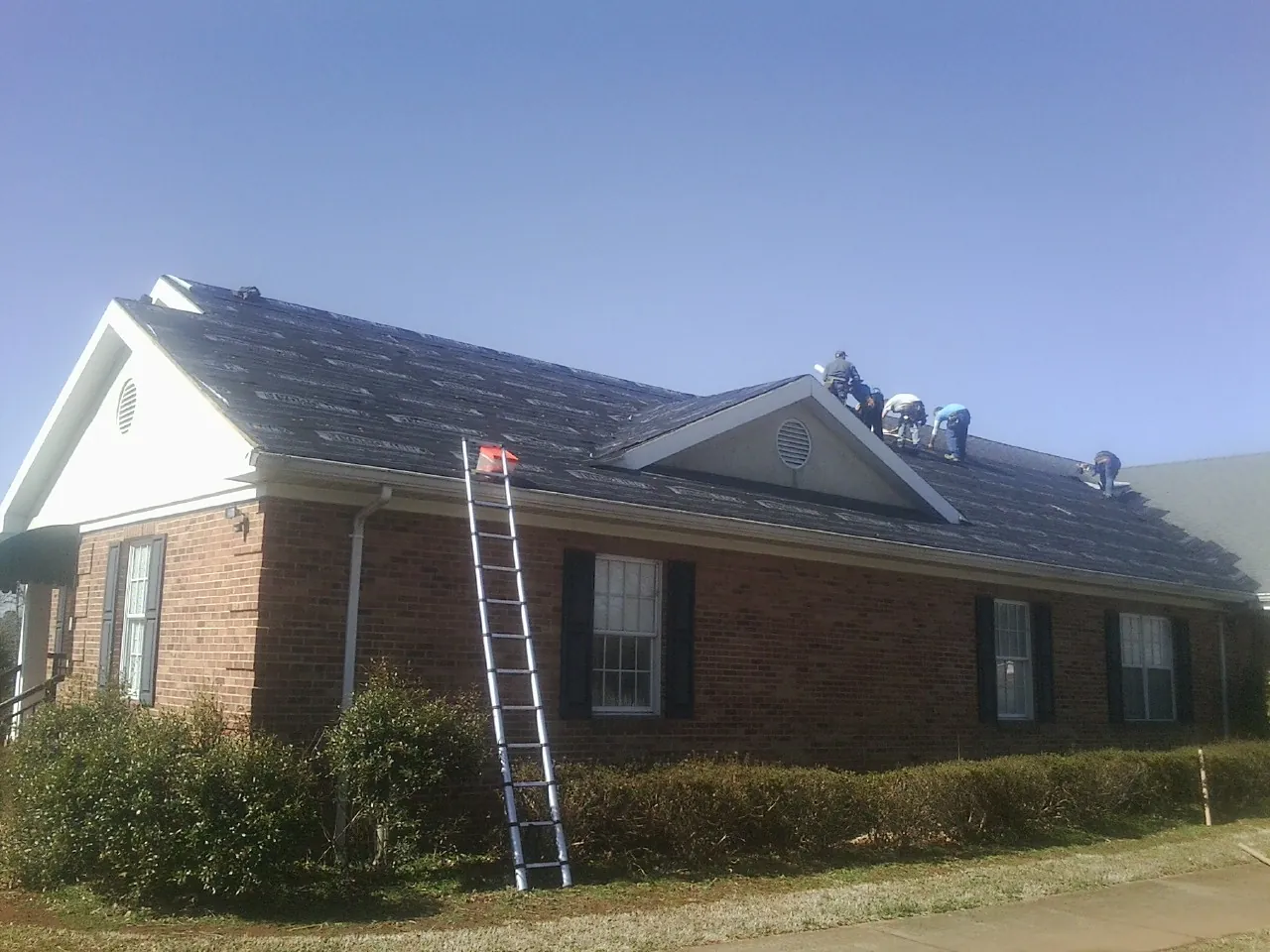 Crew tearing shingles off a brick ranch roof with a ladder set — Emergency Roof Repair work by our crew in Charlotte Hall