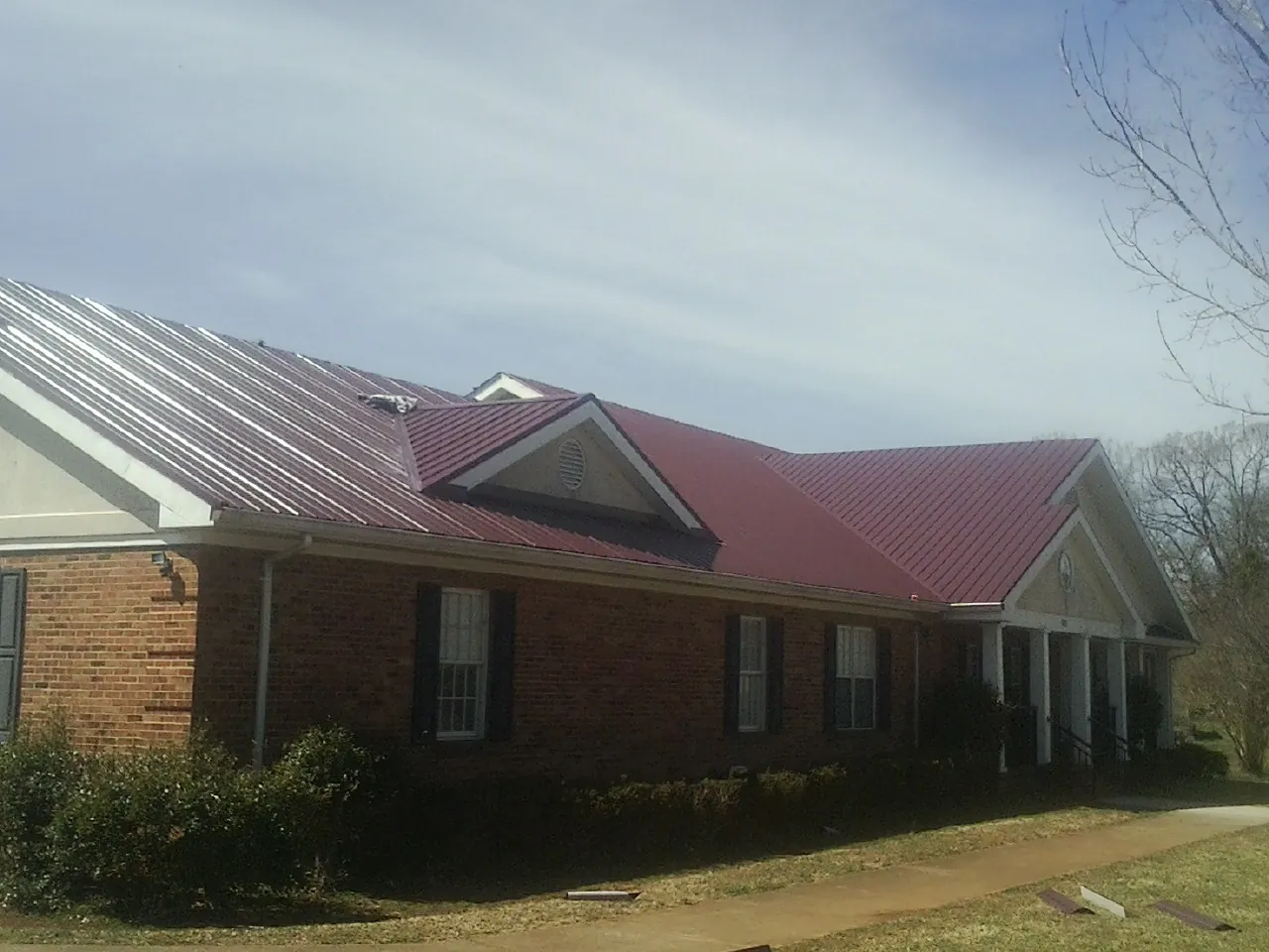 Red metal roof with gabled entries on a long brick building, from a Hail Damage Roof Repair job in Charlotte Hall