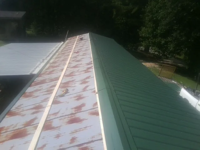 Old rusted panels beside newly installed green metal roofing — Wind Damage Roof Repair by Roofing Brothers in Charlotte Hall