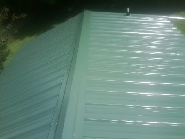New green metal panels meeting at the ridge of a roof — Flat Roof Repair work by our crew in Charlotte Hall