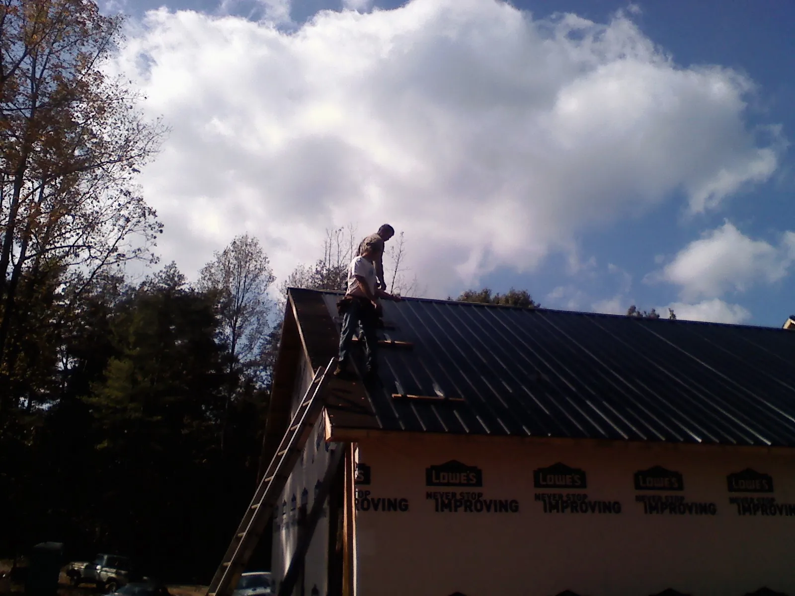 Roofer fastening dark metal panels high against a cloudy sky, from a Roof Inspection job in Charlotte Hall