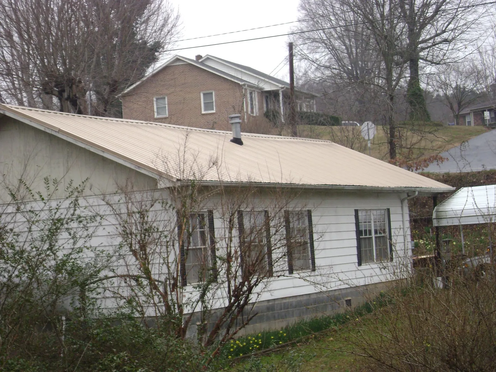 Tan metal roof on a white sided house set into a hillside — Commercial Roofing by Roofing Brothers in Charlotte Hall