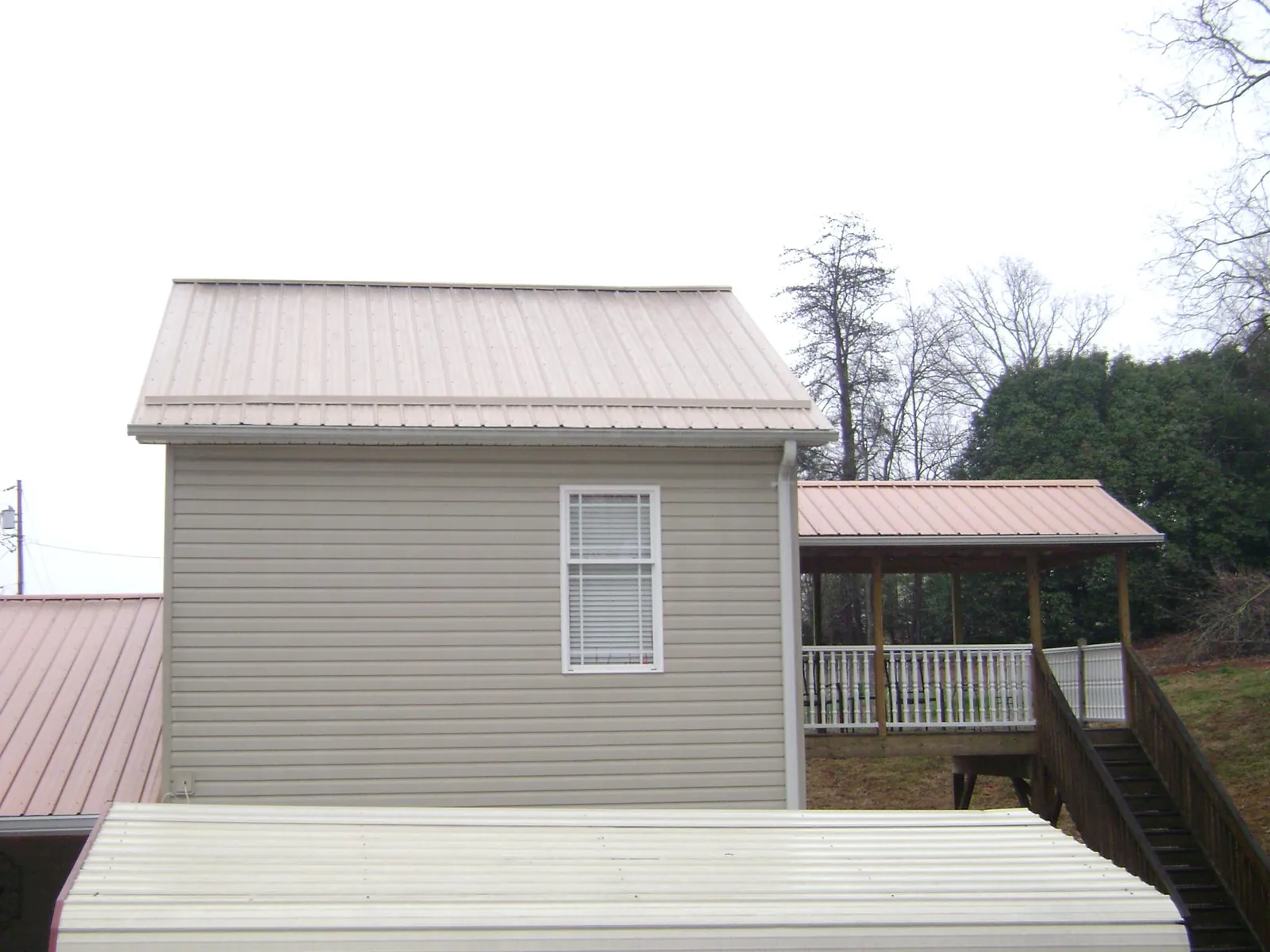 Tan metal roofs on a two story addition and attached porch, from a Roof Replacement job in Charlotte Hall